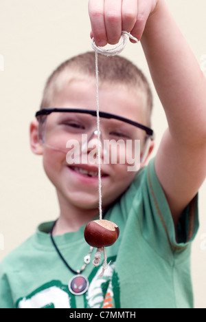 Boy playing Conkers avec des lunettes de sécurité, sur le châtaignier, conkers, décoration, jeu, holding, cheval, horse-chestnut, isolé, Banque D'Images