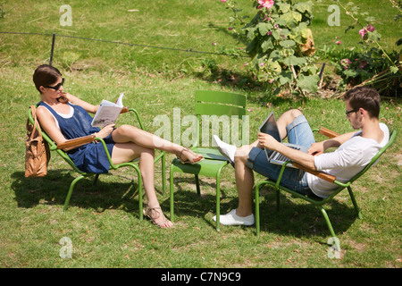 L'homme à l'aide d'un ordinateur portable avec une femme lisant un magazine dans jardin, jardin des Tuileries, Paris, Ile-de-France, France Banque D'Images