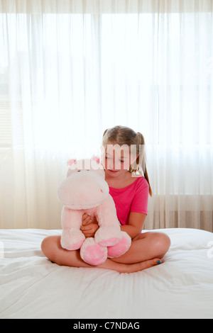 Petite fille assise sur le lit à jouer avec des animaux en peluche Banque D'Images