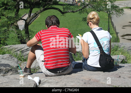 Deux personnes assises sur un rocher la lecture dans un parc Banque D'Images