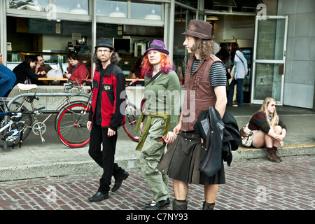 Fille aux cheveux orange & purple hat marche sur Pike Place accompagné de 2 jeunes hommes aux cheveux longs l'un vêtu d'un kilt, en fier grunge de Seattle d'affichage Banque D'Images