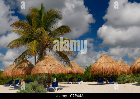 Femme en chaise de plage avec parasols en chaume et de palmiers et blanc les cumulus Riviera Maya Mexique Banque D'Images