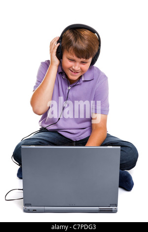 Photo d'un garçon de 11 ans portant des écouteurs assis avec un ordinateur portable, isolé sur un fond blanc. Banque D'Images