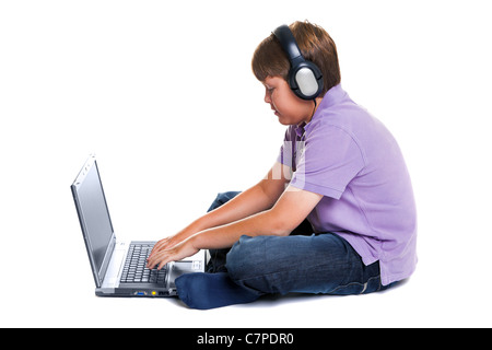 Photo d'un garçon de 11 ans portant des écouteurs assis avec un ordinateur portable, isolé sur un fond blanc. Banque D'Images