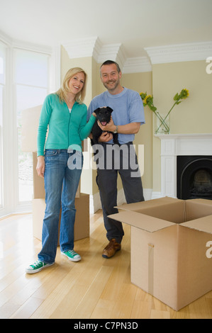 Smiling couple with dog in new home Banque D'Images