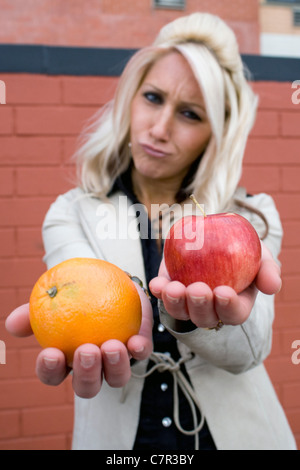 Une jeune femme compare une pomme à une orange. Banque D'Images