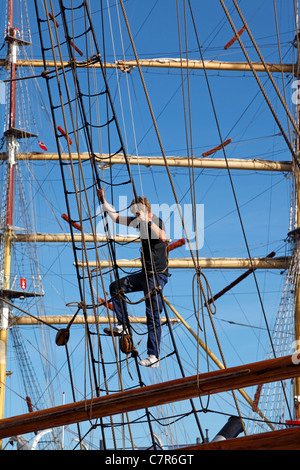 Jeune marin entrant dans le Rig sur Lilla Dan pour travailler dans les hauteurs dans le port de Copenhague. Rig de Dar Mlodziezy en arrière-plan Banque D'Images