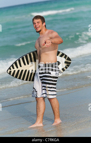 Teenage boy holding skimboard sur la plage, smiling, portrait Banque D'Images