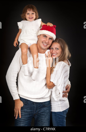 Père in santa hat holding petite fille sur son épaule et l'enlaça sa femme en studio sur un fond sombre Banque D'Images