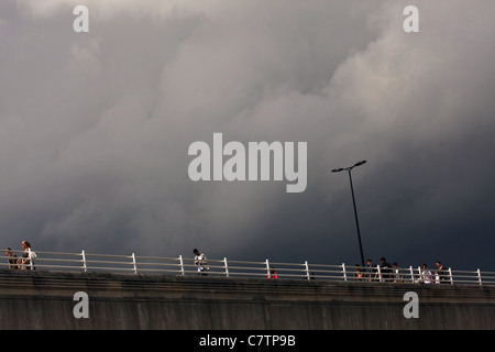 À la recherche jusqu'à personnes traversant Waterloo Bridge, Londres, sous le soleil mais avec des nuages menaçants à passage Banque D'Images