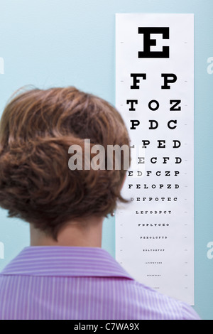 Photo d'une femme à l'opticien d'avoir ses yeux testés à l'aide d'un tableau pour voir si elle a besoin de lunettes. Banque D'Images