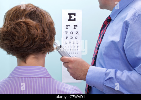 Photo d'une femme à l'opticien d'avoir ses yeux testés à l'aide d'un tableau pour voir si elle a besoin de lunettes. Banque D'Images