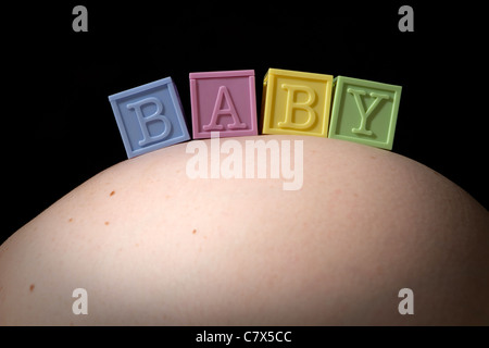 Quatre blocs colorés bébé lettres épeler le mot bébé comme ils sont assis sur une femme enceinte est abdomen gonflé. Banque D'Images