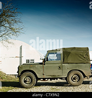 1970 Land Rover Defender Profile tourné sur une journée ensoleillée à l'extérieur une Nissan Construction de huttes. Vert armée avec un toit. Banque D'Images