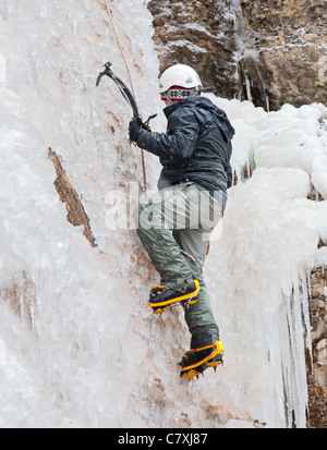 Homme avec piolets et crampons d'escalade sur cascade de glace Banque D'Images