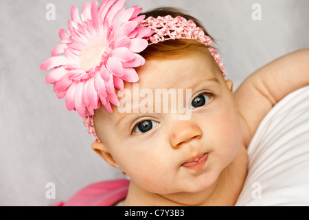 Adorable bébé fille aux yeux brillants qui posent avec une fleur rose band Banque D'Images