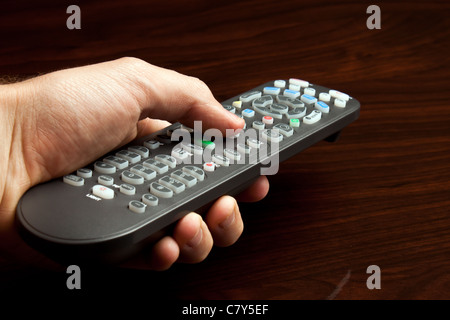 Main pointant à distance de la télévision contre la surface en bois Banque D'Images