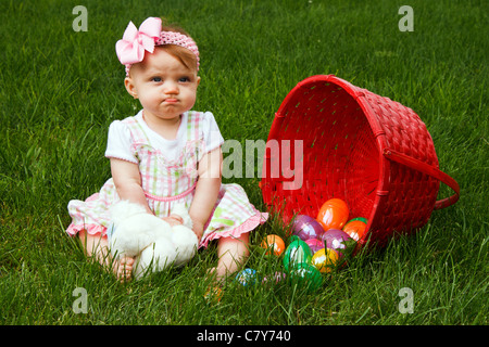 Baby Girl fronçant à côté d'un panier d'oeufs de Pâques renversé Banque D'Images