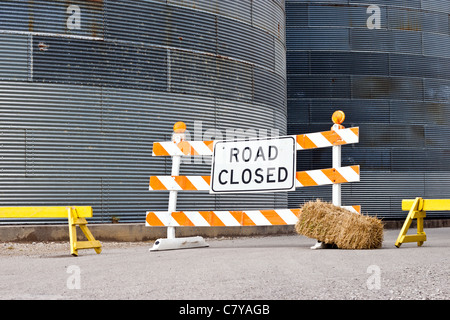 Road closed sign alourdis avec hay sous caution en face de silos Banque D'Images