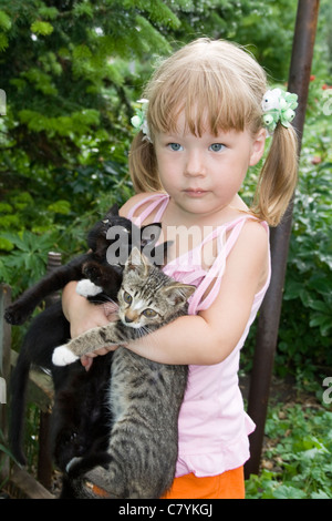 Petite fille embrasse par mains trois chatons Banque D'Images