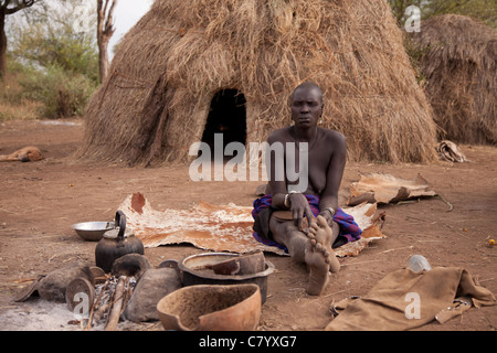Personnes âgées Mursi woman sitting on vache en face de hut, Jinka, vallée de l'Omo, Ethiopie, Afrique Banque D'Images