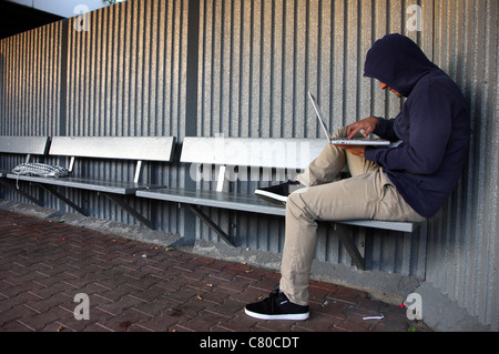 En informatique, hacker, siège de conspirateur, à l'extérieur, dans un abri-bus, avec un ordinateur portable. Photo symbole, de la criminalité sur Internet. Banque D'Images