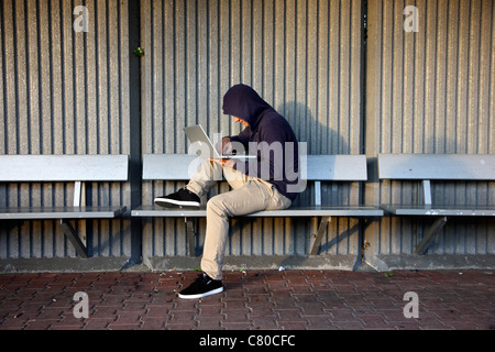 En informatique, hacker, siège de conspirateur, à l'extérieur, dans un abri-bus, avec un ordinateur portable. Photo symbole, de la criminalité sur Internet. Banque D'Images