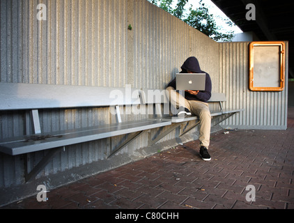 En informatique, hacker, siège de conspirateur, à l'extérieur, dans un abri-bus, avec un ordinateur portable. Photo symbole, de la criminalité sur Internet. Banque D'Images