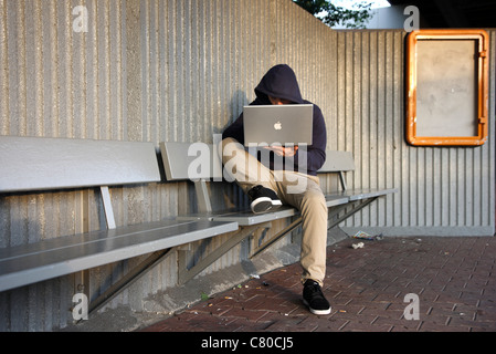 En informatique, hacker, siège de conspirateur, à l'extérieur, dans un abri-bus, avec un ordinateur portable. Photo symbole, de la criminalité sur Internet. Banque D'Images