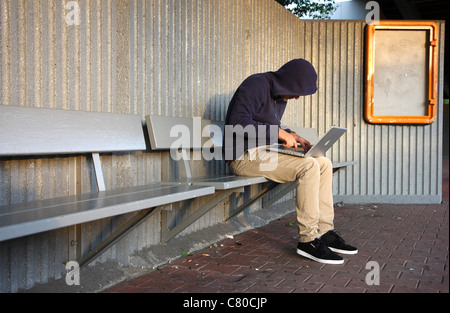 En informatique, hacker, siège de conspirateur, à l'extérieur, dans un abri-bus, avec un ordinateur portable. Photo symbole, de la criminalité sur Internet. Banque D'Images