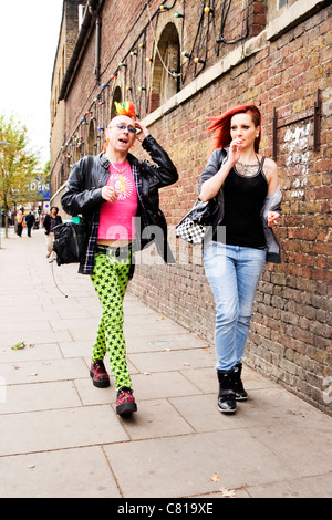 London Camden Town Stables market jeune couple punk il pavé rouge jaune vert rose cheveux t shirt elle cheveux rouge tatouage tats fumeurs Banque D'Images