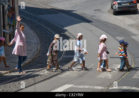 Les enfants de maternelle / maternelle crossing road et de lignes de tramway, d'Alfama, Lisbonne, Portugal Banque D'Images