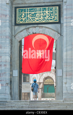 Un visiteur de la mosquée bleue à Istanbul avec un grand drapeau turc accroché au-dessus. Banque D'Images