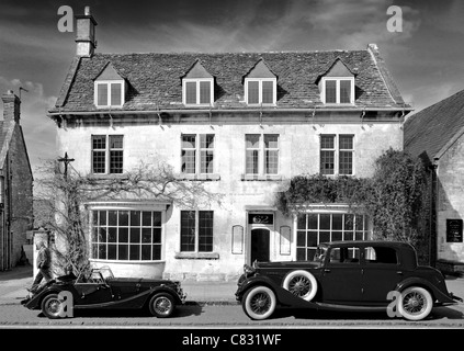 Deux voitures garées à l'extérieur d'un bâtiment historique, Broadway, des Cotswolds. Disponible en couleur et noir et blanc. Banque D'Images