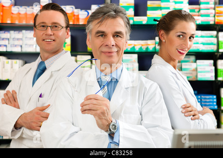 Pharmacien avec son équipe debout dans une pharmacie ou pharmacie en face d'étagères avec des produits pharmaceutiques Banque D'Images