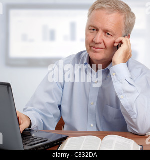 Man talking on phone and smiling in avant de l'ordinateur et la Bible Banque D'Images