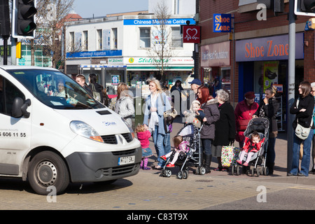 Une foule de piétons se préparer à traverser une route très fréquentée, Loughborough, Angleterre. Banque D'Images