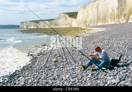 Un amateur de pêche solitaire sur une plage de galets sur un fond de falaises de craie à Berling Gap sur la côte sud de l'Angleterre, Royaume-Uni Banque D'Images