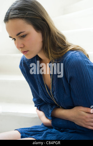 Jeune femme serrant l'estomac, regardant vers le bas dans la pensée Banque D'Images