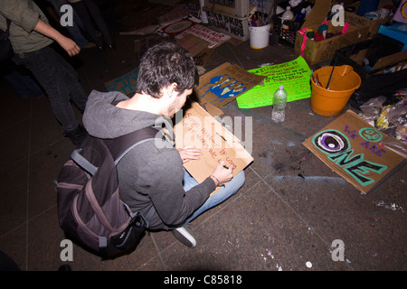 Un "Occupy Wall Street" se trouve sur le terrain protestataire de Zuccotti Park la nuit et peint un signe pour le jour suivant, Banque D'Images