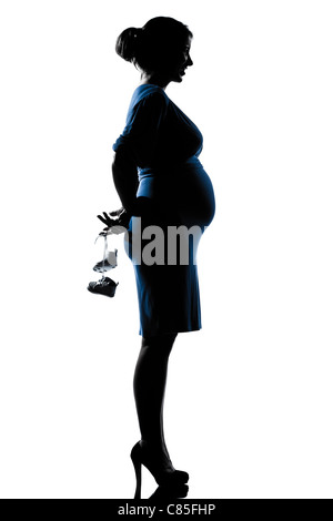 Belle caucasian pregnant woman holding baby shoes en silhouette sur fond blanc isolé studio Banque D'Images