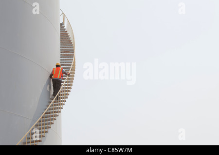 Mixed Race worker climbing escalier sur cuve de stockage Banque D'Images