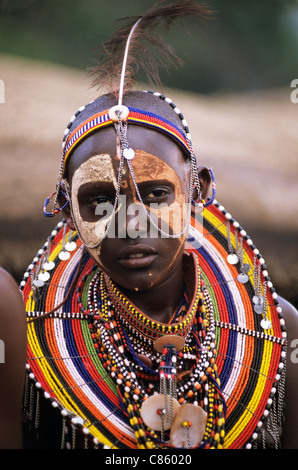 Lolgorian, au Kenya. Manyatta Masaï Siria ; la femme en blanc et l'ocre rouge la peinture pour le visage, des parures de perles. boucles d'oreilles et bracelets. Banque D'Images