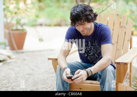 Mixed Race man sitting in chair using cell phone Banque D'Images