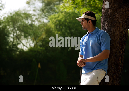 Golfeur appuyé contre un arbre Banque D'Images