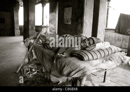 Une femme mourante se trouve sur un lit dans un bâtiment abandonné, Varanasi, Inde Banque D'Images