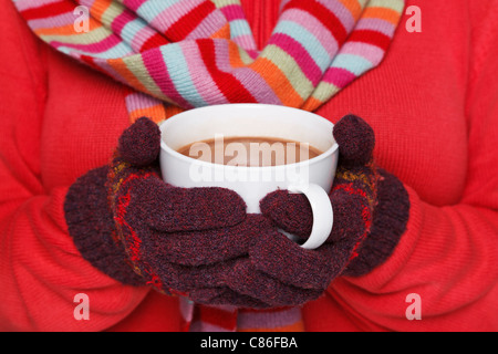 Close up camee photo d'une femme portant un cavalier rouge, des gants de laine et une écharpe tenant une tasse pleine de chocolat chaud Banque D'Images