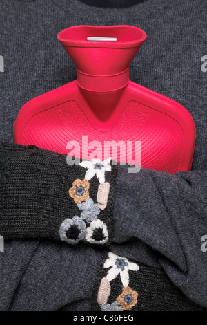 Photo d'une femme tenant une bouteille d'eau chaude rouge sur sa poitrine tout en portant des gants de laine main kniited essayant de garder au chaud Banque D'Images