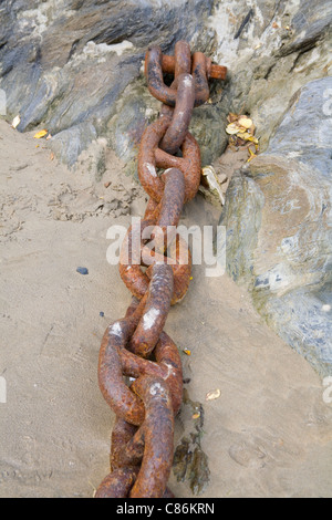 UK chaîne rouillée link attaché à un rocher et allongé sur une plage de sable Banque D'Images