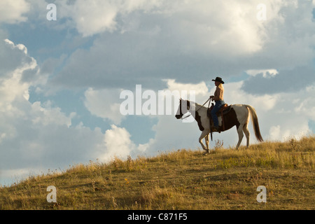 Cowgirl solitaire contre un ciel assombri au crépuscule assis sur un cheval Banque D'Images